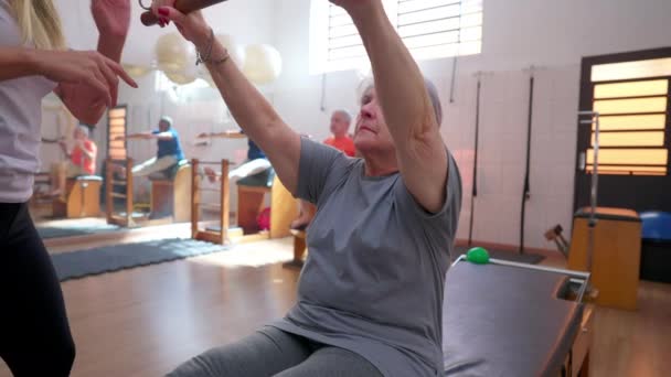 Instruktor Pilates Pomaga Starszej Kobiecie Rozciąganiu Ćwiczenia Podczas Sesji Rehabilitacyjnej — Wideo stockowe