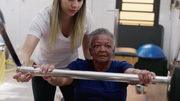 女普拉多教练帮助一位黑人老年妇女使用机器 老年锻炼 柔韧和强壮的身体 — 图库视频影像