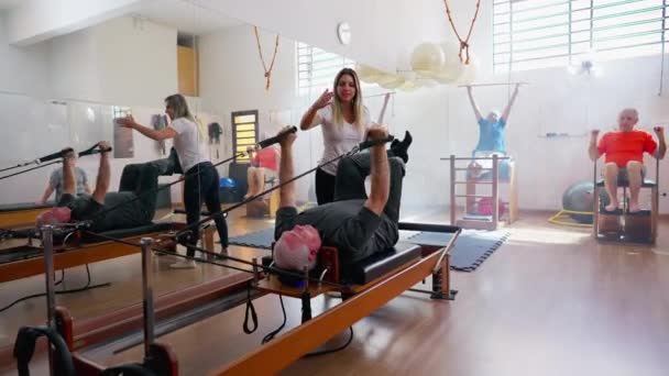 普拉多老年人集体健身课 教练引导一位老年人使用健身器械来伸展和锻炼身体 — 图库视频影像