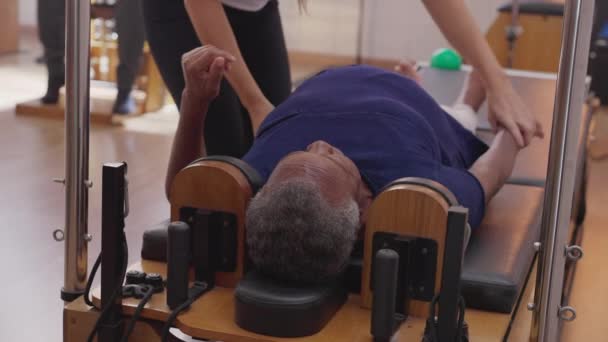 女普拉多教练帮助一位资深妇女使用机器来获得灵活性和力量 老年人的日常锻炼 老年生活方式的幸福 — 图库视频影像