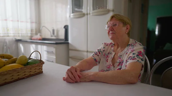 Mujer Anciana Contemplativa Sentada Cocina Casa Mirando Con Expresión Pensativa —  Fotos de Stock