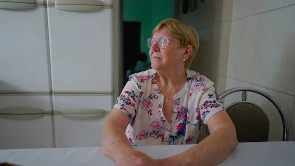 Kontemplacyjna Starsza Kobieta Siedząca Domu Patrząca Przez Okno Kuchni Zagubiona — Zdjęcie stockowe