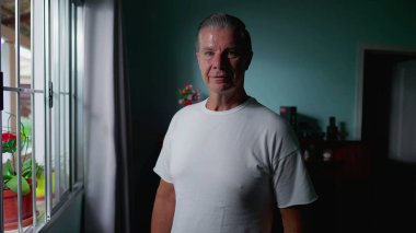 Orta yaşlı bir adamın portresi. Pencerenin önünde dikilip kameraya bakıyor. Yurtiçi gerçek insan yaşam tarzı