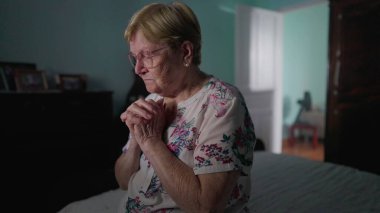 Dindar yaşlı kadın, dua ederken yatağının yanında oturuyor. UMUTAN yaşlı bayan yatak odasında Tanrı 'ya dua ediyor, gerçek hayat ev hayatı FAITH' te yaşlılığı resmediyor.