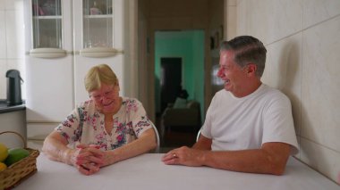 Kıdemli anne, sıradan bir aile hayatı sahnesinde yetişkin oğluyla konuşurken gülümsüyor ve gülüyor. Gerçek hayattaki insanlar ev mutfağında iletişim halindeler.