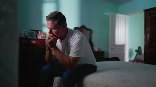 stock image Depressed man sitting by bedside in bedroom. Sad unhappy person looking down suffering from mental illness