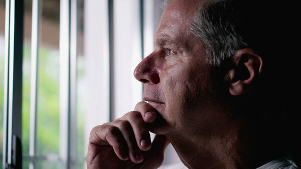 Pensive Middle-Aged Man with Gray Hair Looking Out Window, Contemplative Expression Suggesting Deep Thought about Life, person remembering past memories with hand in chin