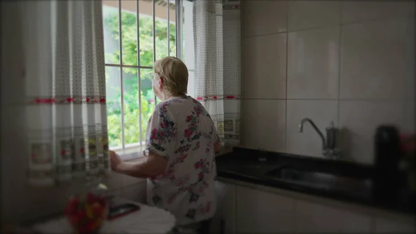 台所に立つ年配の女性のカーテンを開ける 先輩女性の朝の儀式は一日のルーチンを開始し ビューを見て — ストック写真