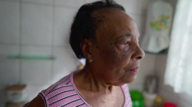 Endişeli son sınıf öğrencisi bir kadın mutfakta pencerenin önünde dikilirken endişeli ve endişeli hissediyor. Endişeli Afrikalı Amerikalı yaşlılar için yakın çekim yüzü