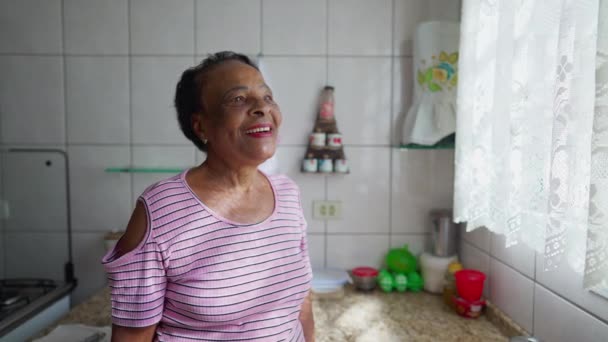 快乐的老妇人站在厨房的窗前向外看 一个面带笑容的黑人老年美国人 — 图库视频影像