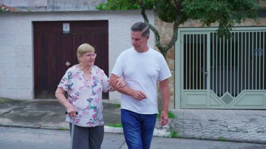 Orta yaşlı bir oğul yaşlı bir anneye yürümesi için yardım ediyor. Bir erkek son sınıf öğrencisini önemser ve destekler. Yaşlılık ev hayatı rutini