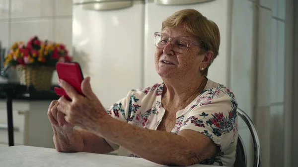 家庭厨房中使用手机装置的老年妇女 — 图库照片