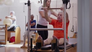 Pilates eğitmeni yaşlı bir adamın makine, egzersiz, sağlık ve sağlık yaşam tarzını kullanmasına yardım ediyor.
