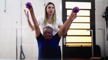 Kadın pilates eğitmeni, siyah yaşlı bir kadına ağırlık çalışması için koçluk yapıyor. Yaşlı bir Afrikalı Amerikalı kıdemli kişi egzersiz rutini