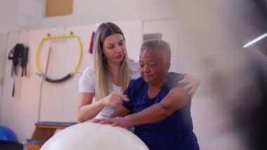 Fizyoterapi Stüdyosu 'nda topta yaşlı Afrikalı Amerikalı kadına yardım eden pilates eğitmeni.