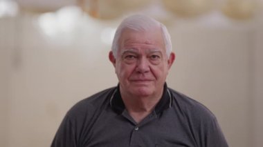 Tarafsız bir ifadeyle kameraya bakan yaşlı bir adam. Beyaz saçlı, yaşlı bir beyaz erkek.