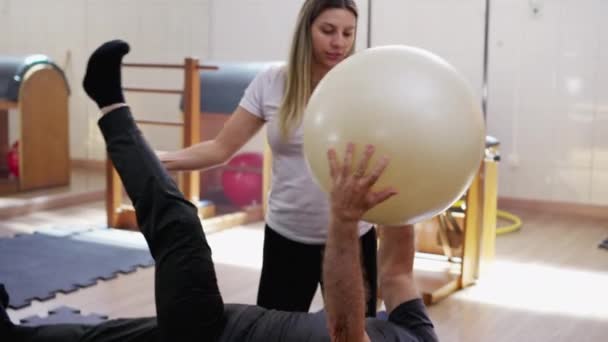 床の上のシニア男性女性理学療法士の指導の下でピラティスボールを練習 高齢者の健康と健康を強調 — ストック動画