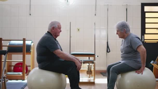 坐在普拉提球上的一对老夫妇笑着 坦诚而真实地交流着老年人的关系 准备锻炼 — 图库视频影像
