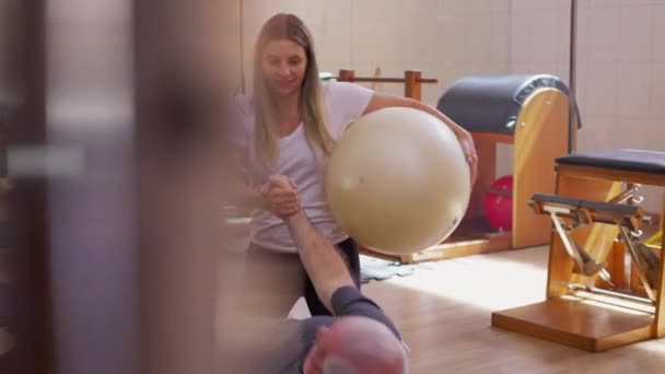 Trener Pilates Pomaga Seniorowi Wstać Podłogi Studiu Fizjoterapii — Wideo stockowe