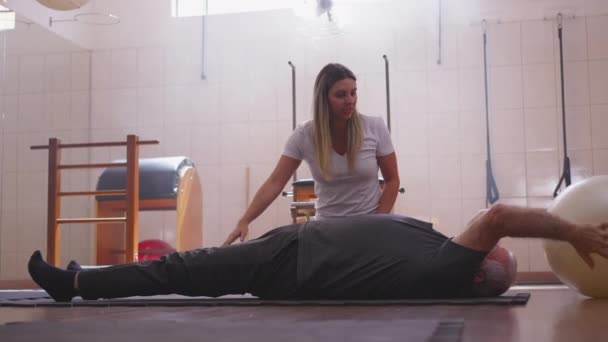 老年人躺在地板上锻炼 普拉提球由女性理疗师指导 老年人日常锻炼 健康和健康概念 — 图库视频影像