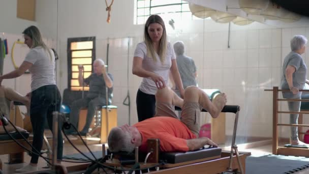 Trener Pilates Prowadzi Starszego Człowieka Maszynach Starsza Osoba Wzmacniająca Ciało — Wideo stockowe