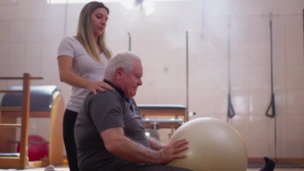 Senior Man Stretching Lichaam Met Pilates Bal Met Hulp Van — Stockvideo
