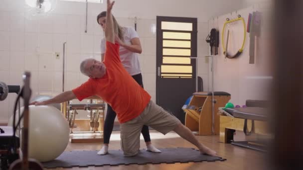 Starszy Mężczyzna Ćwiczący Studiu Pilates Pomocą Trenerki Fizjoterapeuty Starsza Osoba — Wideo stockowe