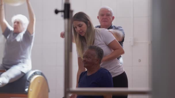 普拉提教师帮助一名巴西黑人老年妇女在理疗室进行举重锻炼 — 图库视频影像