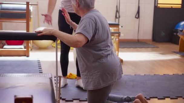 高级妇女在女教练的帮助下从地板上站起来 帮助老年人的年轻妇女 — 图库视频影像
