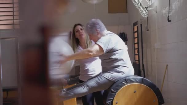 Инструктор Пилатесу Помогающий Пожилой Женщине Тренировках Шаров Способствующий Фитнесу Оздоровлению — стоковое видео