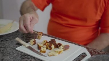 Yaşlı adam kürdanla peynir yiyor, son sınıf öğrencisi tabakta peynir yiyor mutfakta oturuyor.