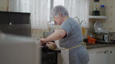 Ev mutfağında pencere kenarında yemek yapan son sınıf öğrencisi bir kadın. Otantik yaşlı bir bayan yemek hazırlıyor.