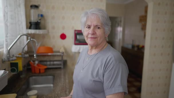 Mujer Mayor Pie Casa Cocina Por Ventana Mirando Cámara Sonriendo — Vídeos de Stock