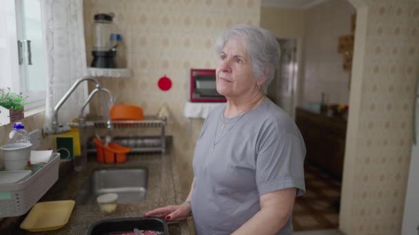 Contemplatieve Senior Vrouw Die Bij Het Keukenraam Staat Met Een — Stockvideo