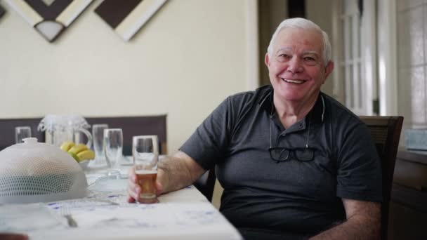 Χαρούμενος Ηλικιωμένος Άντρας Χαμογελάει Στην Κάμερα Καθισμένος Στο Σαλόνι Κρατώντας — Αρχείο Βίντεο
