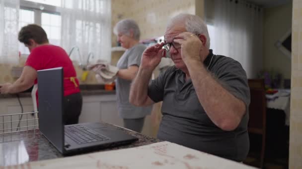 Старший Мужчина Кладет Очки Чтения Использует Ноутбук Кухне Пожилыми Друзьями — стоковое видео