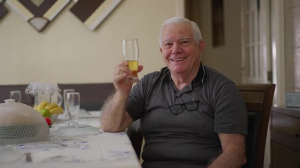 Счастливый Пожилой Человек Пьет Пиво Дома Улыбаясь Камеру Поднимая Стекло — стоковое видео
