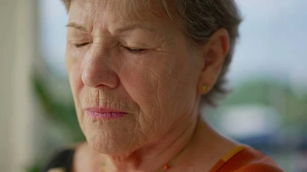 Contemplative senior woman meditating with eyes closed close-up face. An older lady in 70s opening eye awakening
