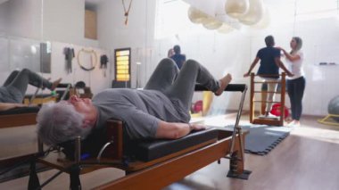 Pilates stüdyosunda egzersiz yapan yaşlı bir kadın. Yaşlı bir Kafkasyalı vücudu esnediği için Makine 'nin üzerine yatmış. 
