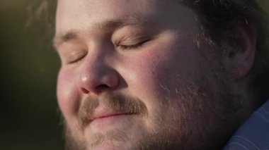 Genç adam meditasyonda gözlerini kapatıyor. Yüzünü kapatıyor. Açık havada parkta oturuyor. Dalgın, beyaz, aşırı kilolu, stressiz ve endişeli bir erkek.