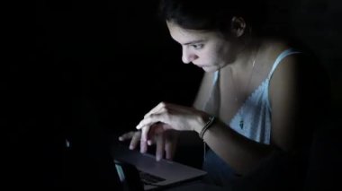 Focused woman typing on laptop keyboard in the dark wearing headphones. Person working in the dark. Modern lifestyle