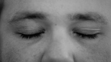 Meditasyonda gözlerini kapayan genç bir adamın monokromatik klipsi. Siyah-beyaz gülümseyen düşünceli bir erkek.