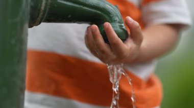 Çocuk elleri, yavaş çekimde parktaki muslukta akan suyla oynarken yakın plan çekimde.
