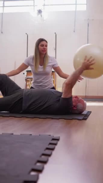 理学療法士のコーチは 高齢の男性にピラティスボール ワークアウトルーチンを使用するように指示します 高齢者運動 — ストック動画