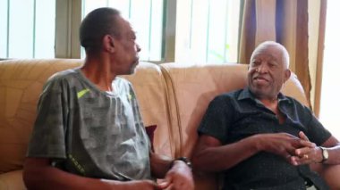 Kanepede oturan yetişkin oğlunu kucaklayan siyahi bir baba. Afrikalı Amerikalı aile üyeleri sevgi ve destek göstererek sarılıyorlar.