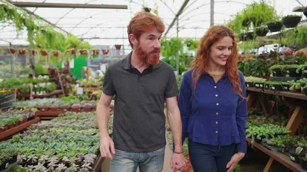 ダイナミックトラッキングで装飾的な植物を探しているフラワーショップ_赤毛のカップルを探索する 花のための若い男と女性のショッピング — ストック写真