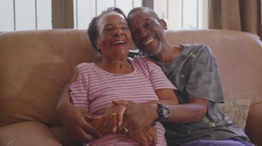 Siyah Brezilyalı yetişkin bir oğul ve yaşlı bir anne kanepeye oturmuş kameraya gülümsüyor. Afro-Amerikan aile yakınları insan portresi
