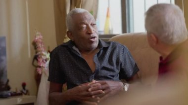 İçtenlikle sunbae evde, kanepede arkadaşlarıyla sohbet ediyor. Afrikalı Amerikalı yaşlı bir erkek otantik gerçek hayat etkileşiminde insanlarla konuşuyor.