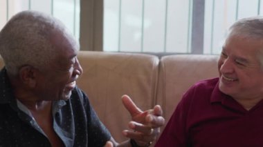 Gerçek samimi etkileşimde gülen ve gülümseyen mutlu ırklar arası arkadaşlar. Gerçek hayatta mutlu insanlar koltukta oturup sohbet ederler.