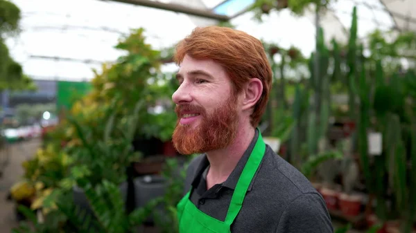 Stock image One Happy young man employee walking through plant store wearing green apron. A caucasian male staff face close-up walks through flower shop isle